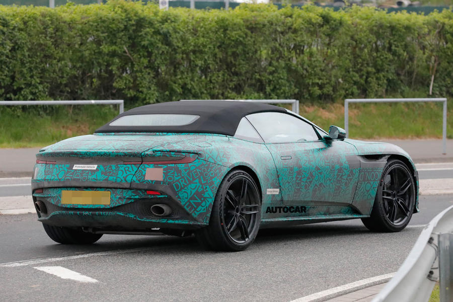 Camouflaged Aston Martin DB12 Volante driving around roundabout, rear end